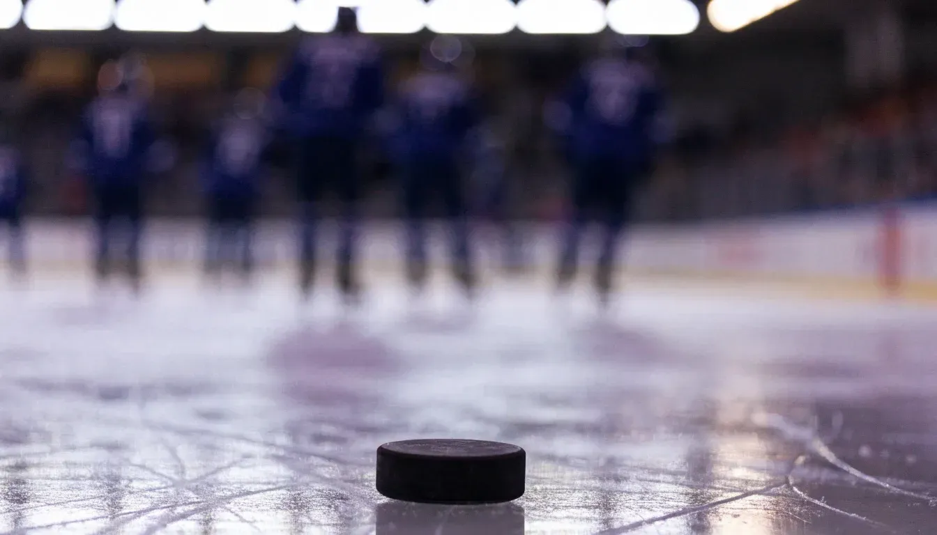 Ein Eishockeypuck liegt in Grossaufnahme auf der Eisfläche, feine Kratzer im Eis glänzen im hellen Hallenlicht.