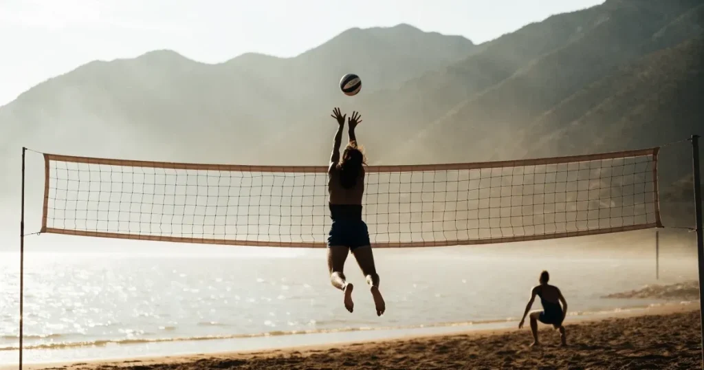 Ein Volleyball liegt am Fuss des Netzes auf Sand, im Hintergrund glitzert ein See und ein Bergzug steht im Dunst.